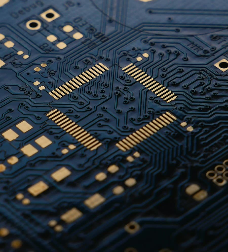 Placa de circuito azul marino a primer plano, con pistas doradas que salen en todas direcciones desde un chip central