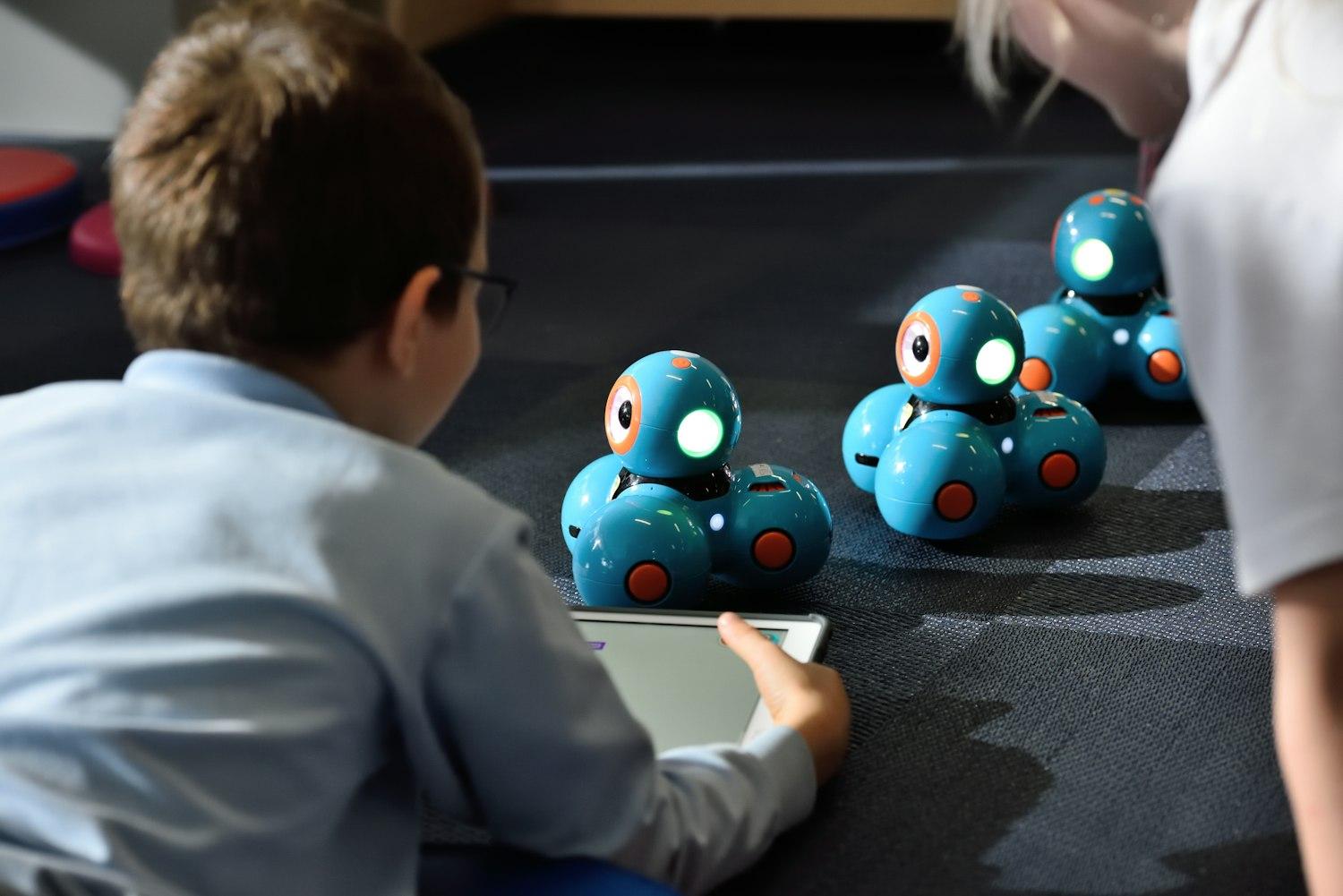 Niño de primaria programando con una tableta unos robots educativos de luz azul